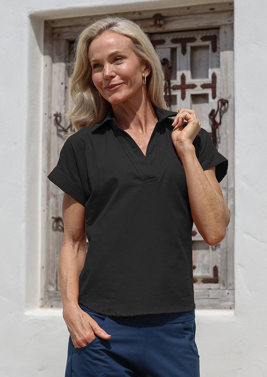 Woman wearing a black cotton relaxed fit top with short sleeves and a collar, paired with blue pants