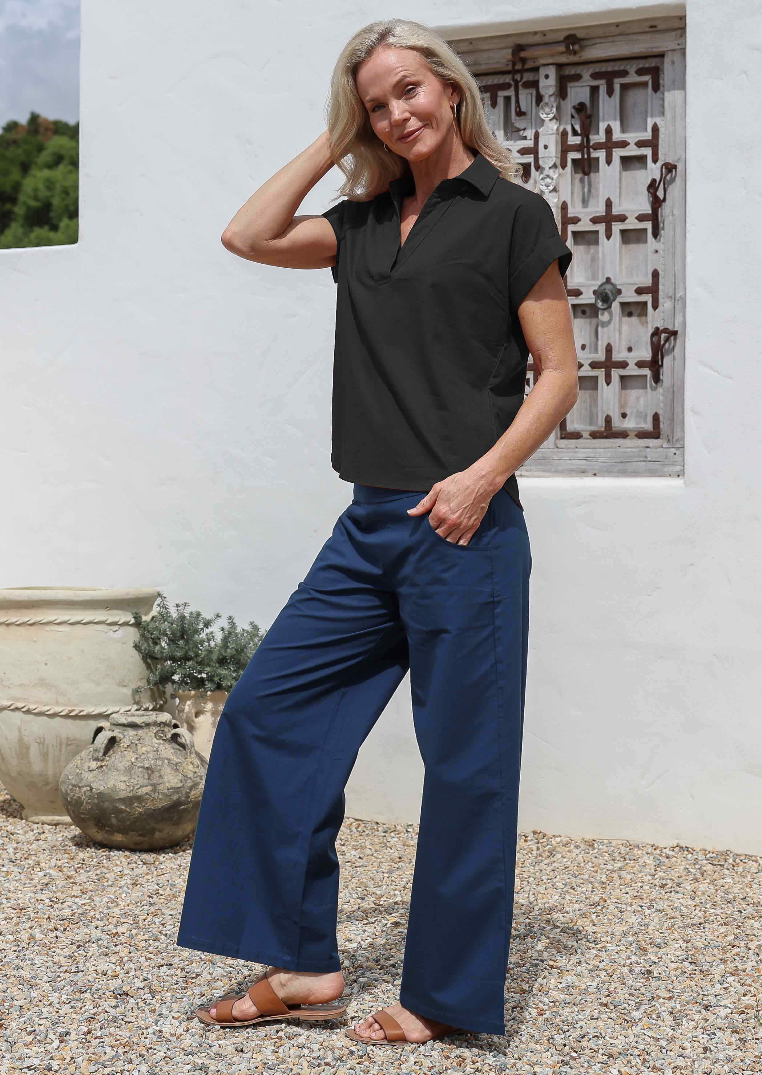 Woman wearing a black relaxed fit cotton top with a collar, paired with long blue pants