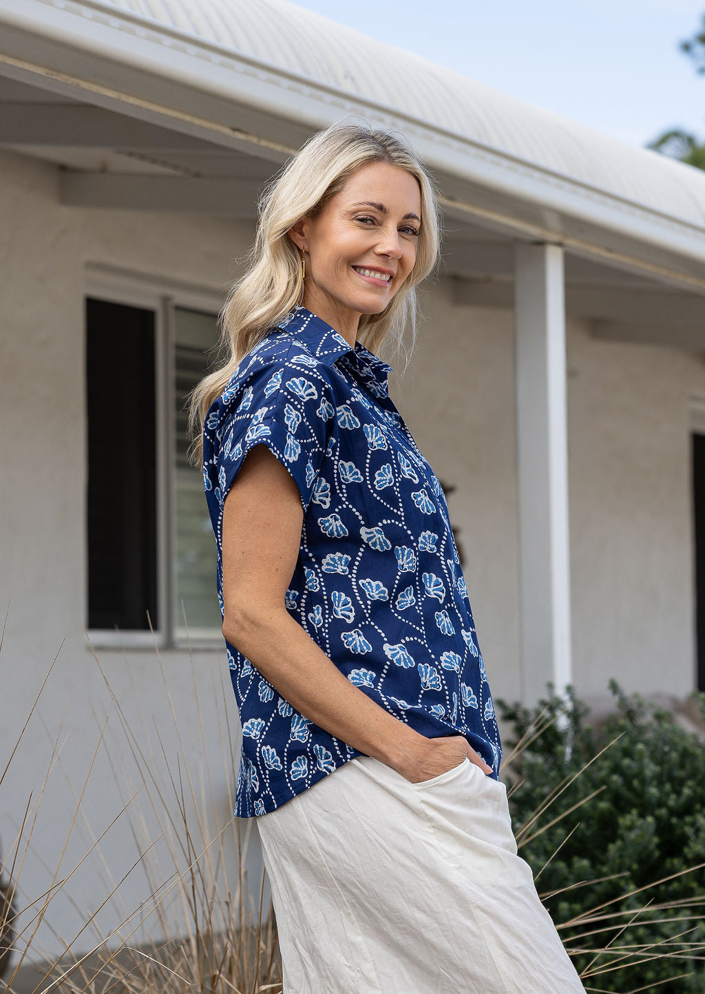Woman standing sideways wearing a floral cotton top with short folded cuff sleeves, collar and V neckline