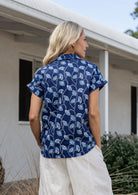 Woman standing backwards wearing a floral cotton top with short folded cuff sleeves, collar and V neckline