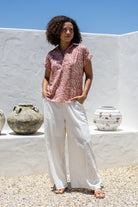 Woman wearing a rose pink based relaxed fit, shirt style floral cotton top with white plain pants.
