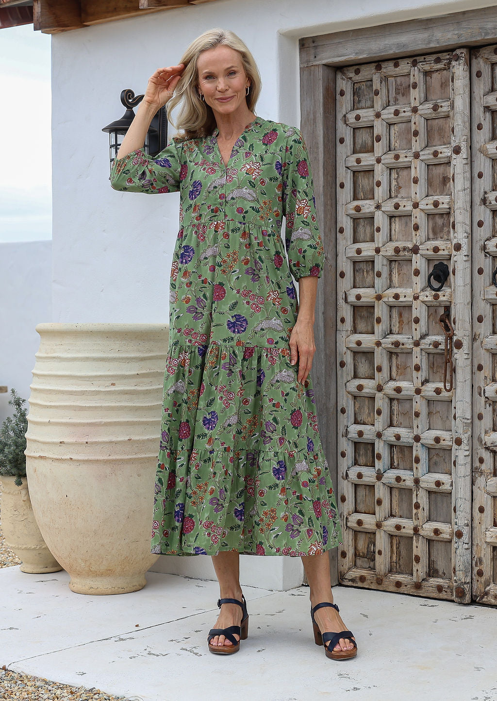 Woman posing in a 100% cotton floral maxi dress with buttoned bodice, mandarin collar and 3 tiered flowy skirt with pockets.