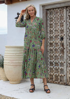 Woman posing in a 100% cotton floral maxi dress with buttoned bodice, mandarin collar and 3 tiered flowy skirt with pockets.
