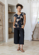 Model posing in a black based floral print tailored cotton top with cap sleeves, round neckline and length sitting at the hip 