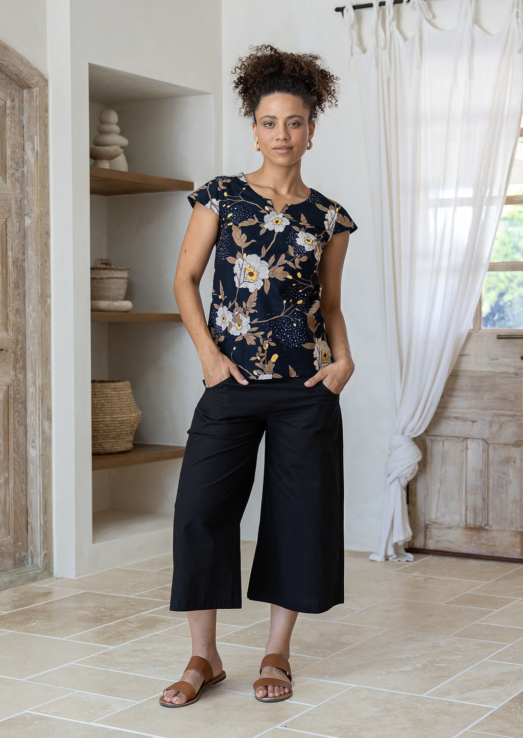 Woman standing in a 100 percent cotton floral print top with cap sleeves, round neckline and keyhole cutout.