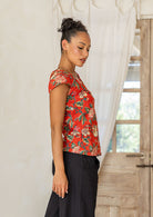 Woman standing in a 100 percent cotton floral print top with cap sleeves, round neckline and keyhole cutout.