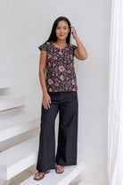 Woman stands wearing a 100% cotton tailored top with cap sleeves and keyhole round neckline.