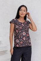 Woman stands against a white background wearing a 100% cotton tailored top with cap sleeves, round neckline and keyhole cutout at the neck.