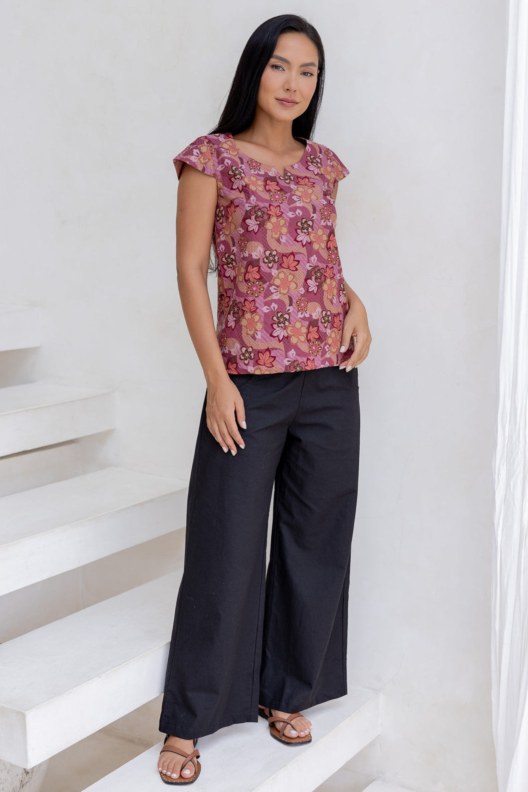 Woman standing in a 100 percent cotton floral print top with cap sleeves, round neckline and keyhole cutout.