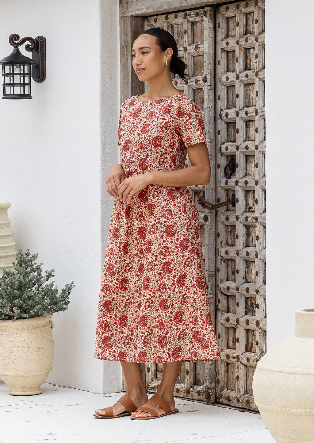 Woman standing wears 100 percent cotton relaxed fit, midlength dress in cream based warm floral print.