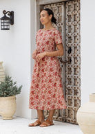 Woman standing wears 100 percent cotton relaxed fit, midlength dress in cream based warm floral print.