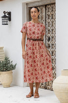 Model stands in relaxed fit cotton sundress with high round neckline, short sleeves in front of a white wall with decorative elements.