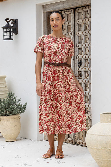 Model stands in relaxed fit cotton sundress with high round neckline, short sleeves in front of a white wall with decorative elements.