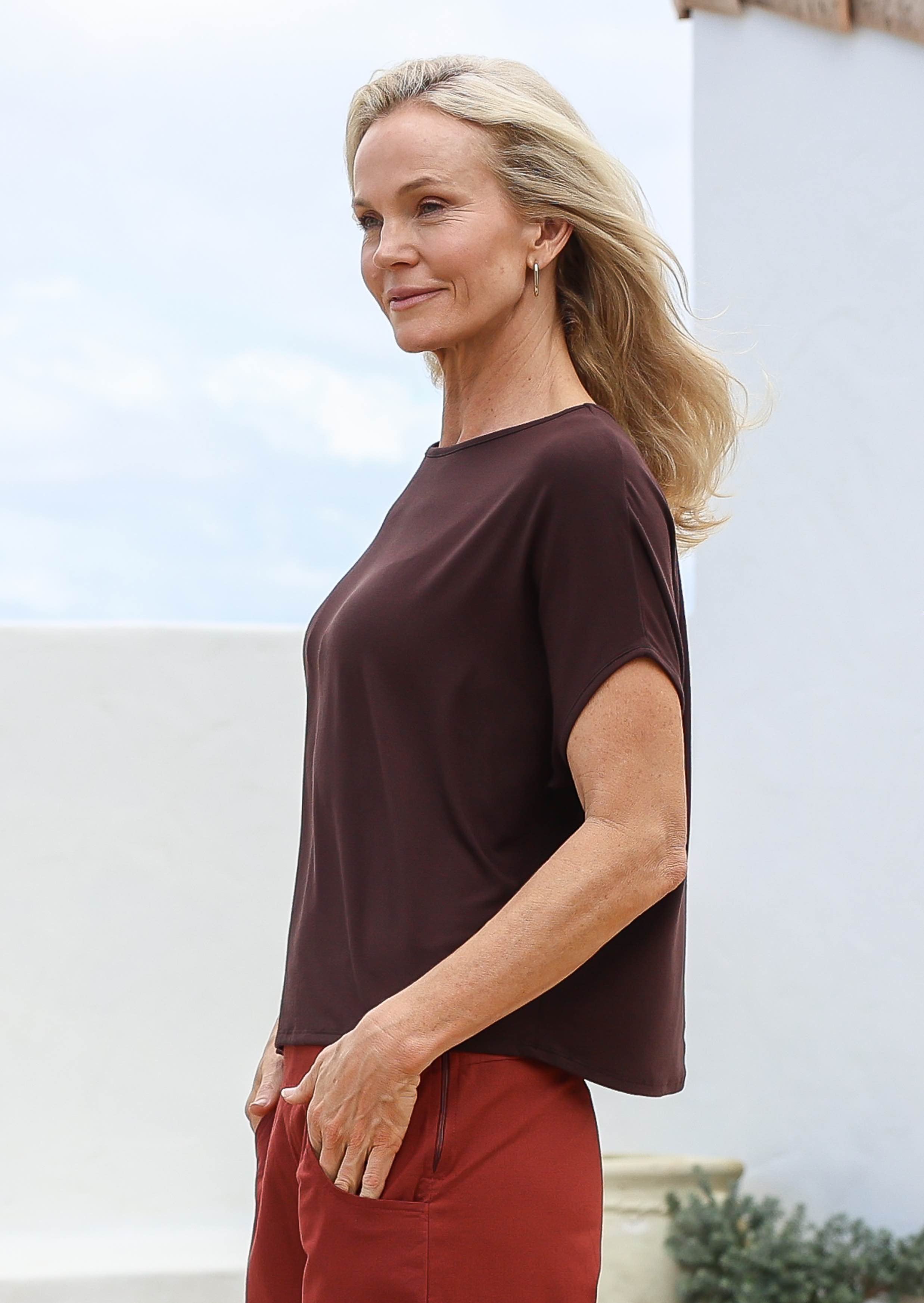 Woman wearing a brown top and burnt henna pants standing outdoors with a light background