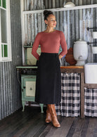 Woman wearing a dusty pink top with a black cotton corduroy A-line skirt paired with tan boots