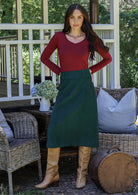 Woman in a red top and green cotton corduroy A-line midi length skirt standing with hands on hips