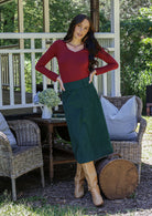 Woman in a green cotton corduroy A-line midi length skirt paired with a red long sleeve top and tan boots