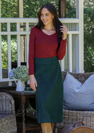 Woman in red top and green cotton corduroy A-line skirt standing outdoors with wicker chairs