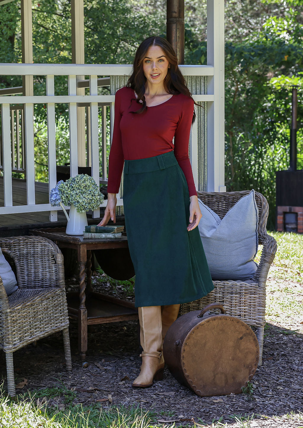Woman in a red long sleeve top and green cotton corduroy A-line midi length skirt next to chairs and a table