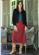 Woman in a red cotton corduroy midi length skirt and black corduroy jacket, paired with a teal top and tan boots