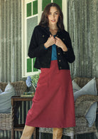 Woman wearing a black jacket, teal top and red cotton corduroy A-line midi length skirt