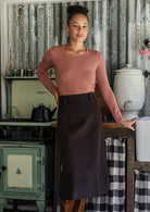 Woman standing with hand on hip wearing a chocolate brown cotton corduroy A-line midi length skirt paired with a rose pink top