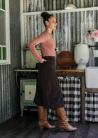 Woman wearing a chocolate brown cotton corduroy A-line midi length skirt with hands in back pockets