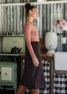 Woman standing side on wearing a chocolate brown cotton corduroy A-line midi length skirt paired with a rose pink top