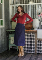 Woman in a red top and blue cotton corduroy midi length A-line skirt standing with hands on hips
