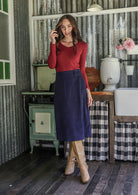 Woman in a red top and blue cotton corduroy midi length skirt with belt loops, paired with tan boots