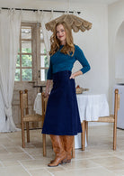 Woman stands sideways wearing a cotton corduroy skirt in navy blue with belt loops and a side zip. 