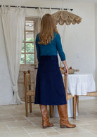 Woman stands backwards wearing a cotton corduroy skirt in navy blue with belt loops and a side zip.