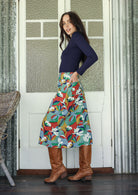 Woman standing sideways wearing a colorful floral cotton skirt with hands in back pockets