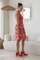 Woman stands sideways in a floral cotton dress with side zip standing in a living room.
