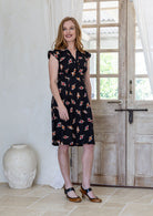 Woman wearing black based floral cotton dress with cap sleeves, box pleats, side zip and V neckline