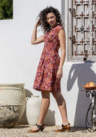 Woman stands sideways in a floral cotton dress with side zip standing outdoors against a wooden wall