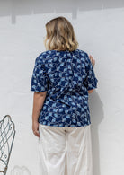 Woman standing backwards wearing a 100% cotton top in navy based floral print paired with white plain pants