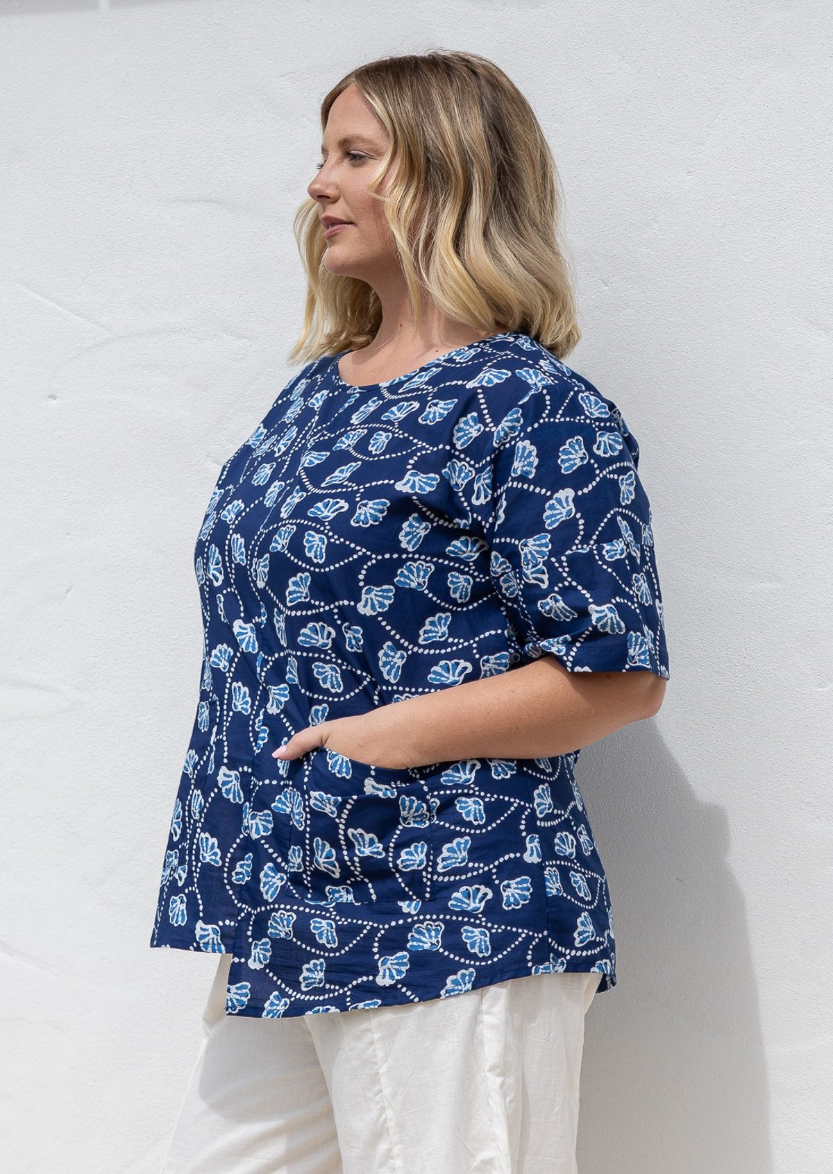 Woman standing wearing a 100% cotton top in navy based floral print paired with white plain pants