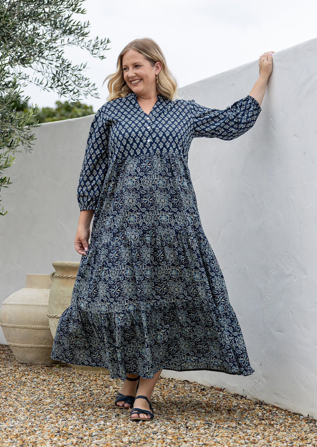 Woman stands in navy blue based floral cotton maxi dress with buttoned bodice, 3/4 sleeves and flowy three tiered maxi skirt
