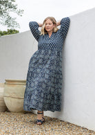Woman standing in navy blue based 100% cotton flowy tiered maxi dress with 3/4 sleeves, buttoned bodice and pockets 