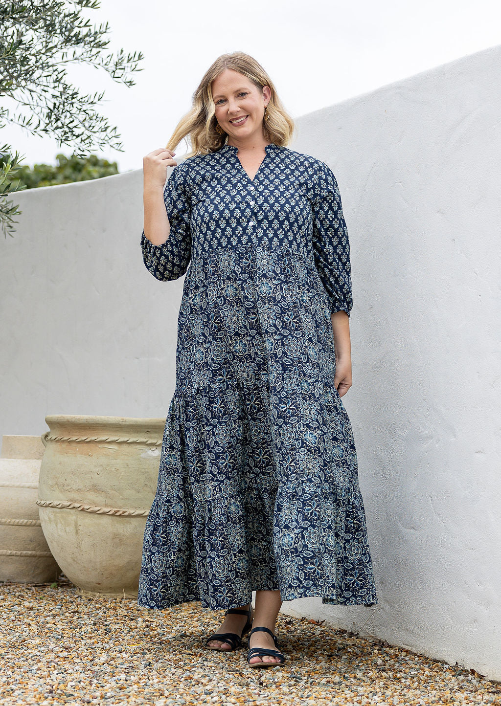 Woman wearing a 100% cotton tiered maxi dress in navy blue based floral print against a white wall 