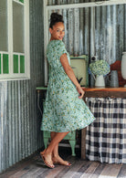 Woman in a pale green cotton floral dress standing side on showing the back cinched with shoestring ties