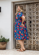 Woman in a navy based colourful floral dress standing side on showing the back cinched with shoestring ties