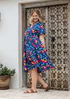 Woman standing sideways wearing a 100% cotton dress in royal blue based floral print