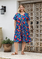 Woman wearing a royal blue based cotton floral button through dress with both hand in pockets, short sleeves and a V-neckline