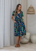 Woman wearing a navy based blue cotton floral button through dress with both hand in pockets, short sleeves and a V-neckline