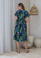 Woman in a navy based cotton floral dress standing in a room showing the back of the dress cinched with shoestring ties