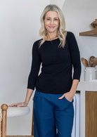 Woman wearing a rayon boat neck black 3/4 sleeve top paired with plain pants
