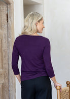 Woman standing backwards wearing a rayon boat neck purple 3/4 sleeve top