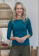 Woman wearing a rayon boat neck teal 3/4 sleeve top standing in a kitchen setting